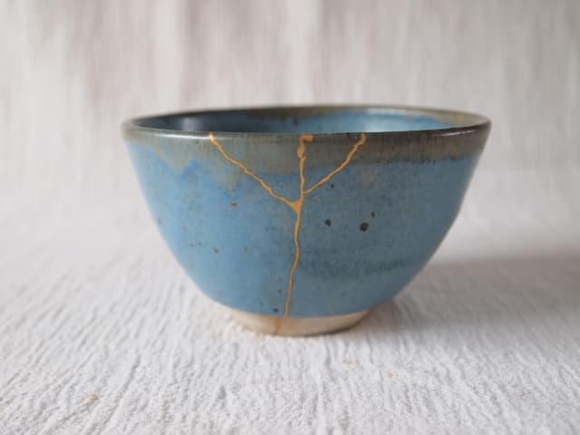 Kintsugi artisan hands applying gold powder to lacquer repair line on ceramic bowl