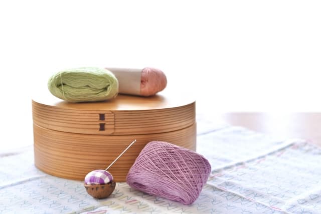 Sashiko tools arranged on wooden surface — long needle, thread cards, thimble in natural light