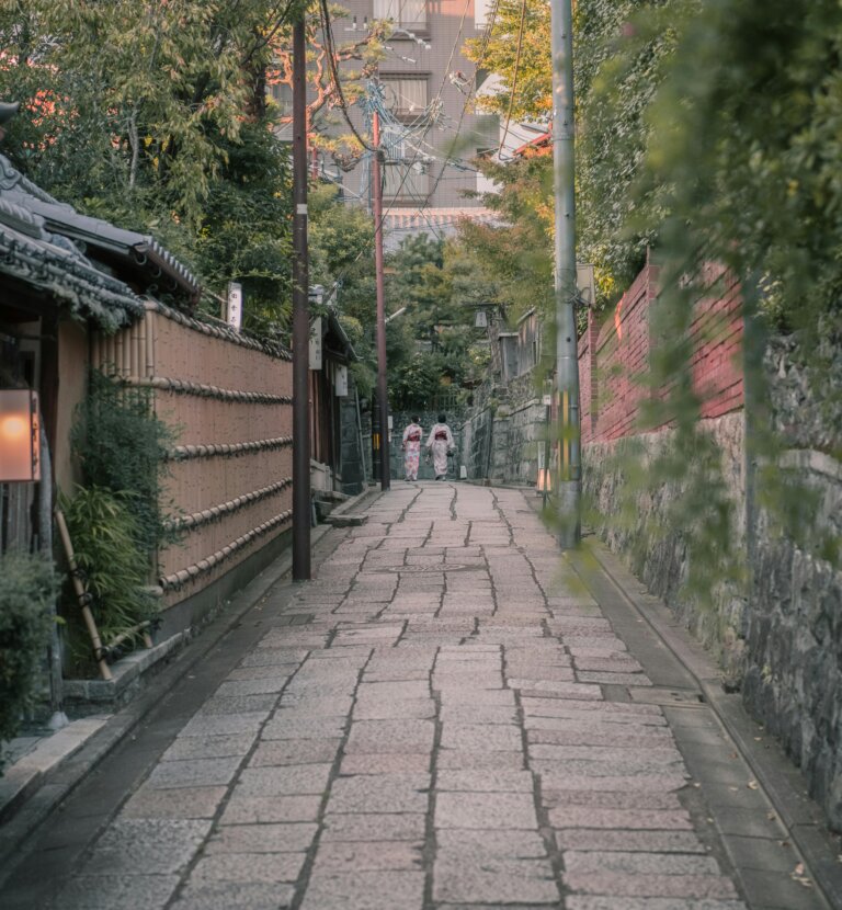 Scenic view of women in kimonos walking on a historic stone path in Kyoto, Japan.