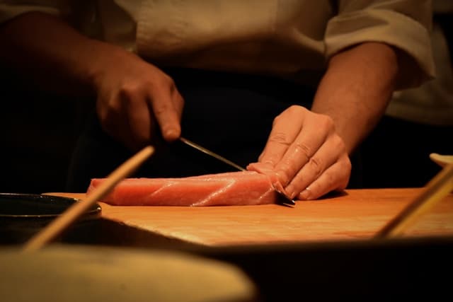 Japanese chef slicing raw fish precisely with a long kitchen knife