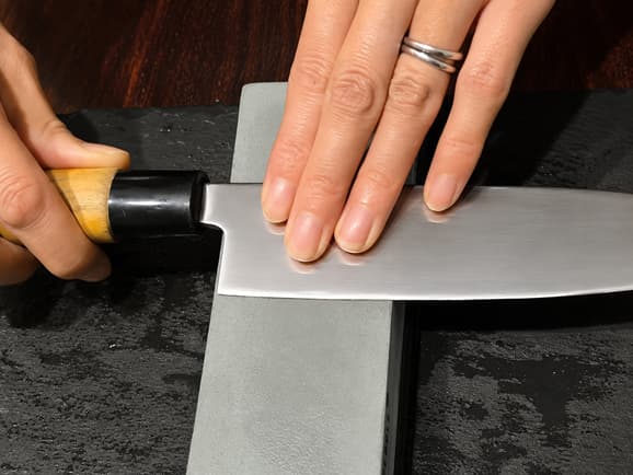 The Whetstone and the Edge Japanese knife rotated to 90 degrees on a whetstone to sharpen the heel area near the handle