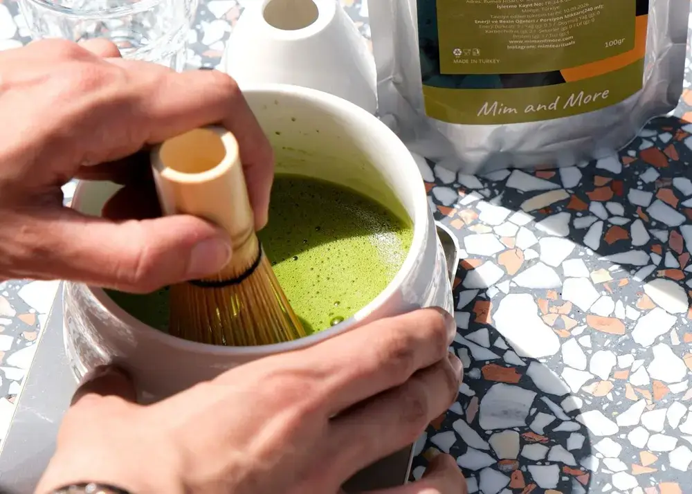 What I Learned Before Making Matcha at Home Hand whisking matcha tea outdoors on a terrazzo table